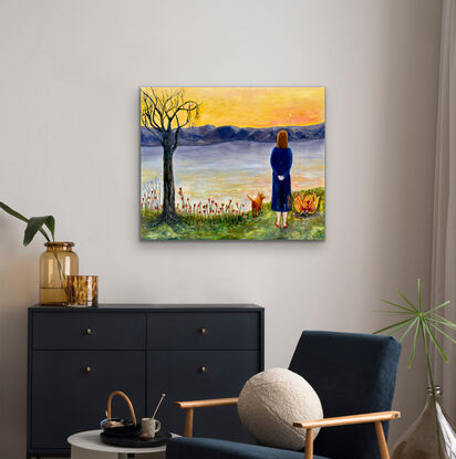 A woman and her animal companion look across water to the mountains and evening sky