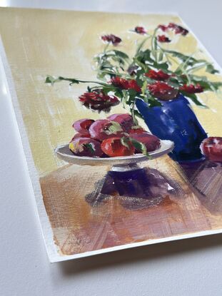 Backlit Red dahlias in a dark vase with a bowl of apples casting a shadow forward