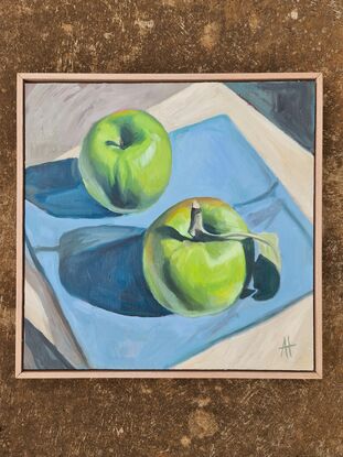 Looking from above onto two green Granny Smith apples on a blue cloth.