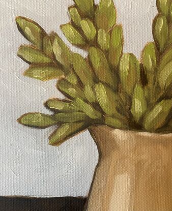 Green foliage in a mustard jug on a neutral background.