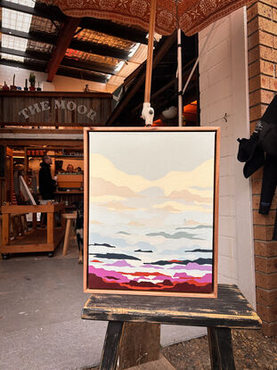 an abstract painting of a cloudy sky, depicting the sunset. Large cream and white clouds turn into scattered blue, pink, red, purple, dark blue and orange clouds. A tiny silhouette of a surfer can be found surfing one of the clouds, like it's a wave. the painting is framed in reclaimed Tasmanian Oak timber.