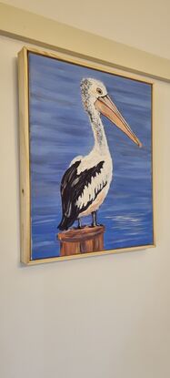 A pelican stands on a post overlooking the water.