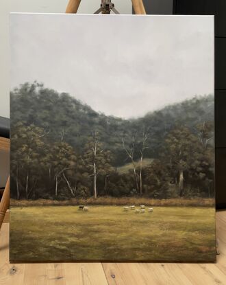 Flock of sheep in the foreground of a dramatic Australian landscape dense with gum trees.