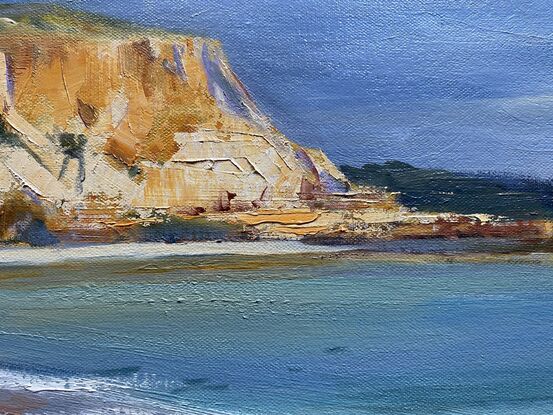 Textured, ochre cliffs against deep blue waters with sandy beach. 