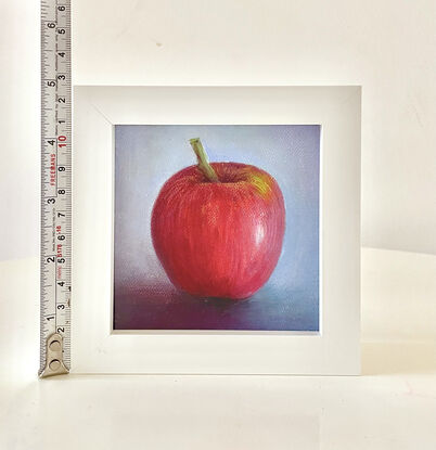 A small painting of a red apple with a blue background on a framed canvas.