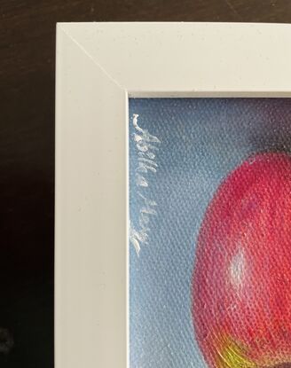 A small painting of a red apple with a blue background on a framed canvas.