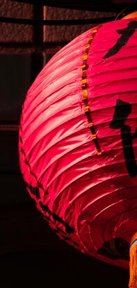 A red lantern is highlighted from the sunrise, it is set against a shadowy wall where many, small tiles can just be seen in the dark.