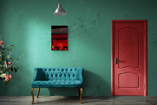 A collection of red, glowing lanterns hangs from the underside of a concrete ceiling. Above is the gritty face of the concrete building, intersected vertically with metal sheets.