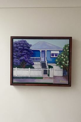 Typical blue Queenslander style home found in Brisbane. It is surrounded by. frangipani tree and a Jacaranda tree common in Brisbane. All neatly behind a white picket fence. 