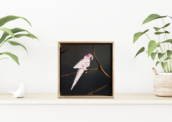 An origami parrot, with a cherry blossom pattern, perched on a bare branch. 