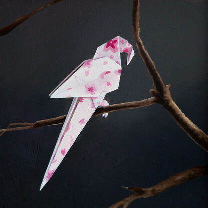 An origami parrot, with a cherry blossom pattern, perched on a bare branch. 