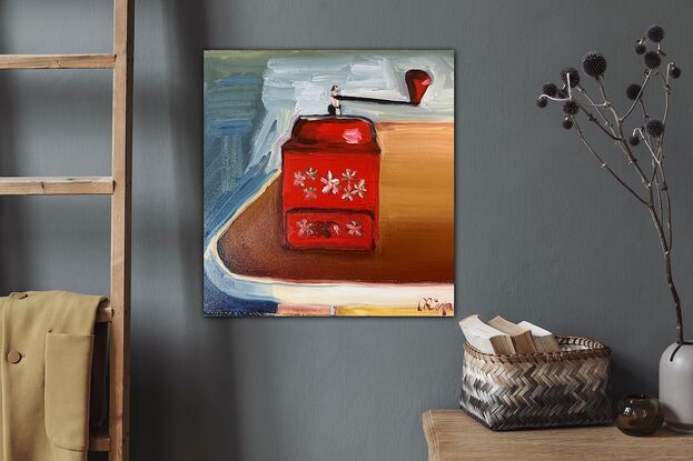 An antique coffee grinder on a 1950’s table. Red in colour with white daisies on it, sitting on a brown table with a blue grey and white background.