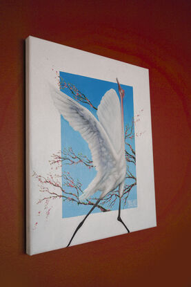 A painting of a white crane in mid-flight with wings outstretched, set against a vibrant blue background. The bird is surrounded by branches adorned with delicate pink blossoms, creating a serene and elegant composition.