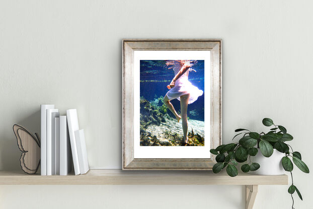 Young woman spinning underwater in white dress whilst standing on the sandy floor.