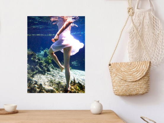 Young woman spinning underwater in white dress whilst standing on the sandy floor.