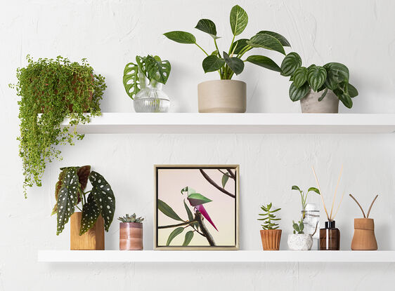 A purple and pink origami parrot perched on a bare branch with purple flowers growing. 