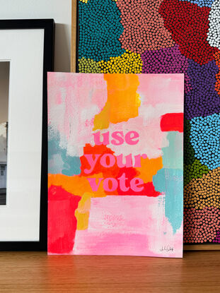 abstract acrylic painting with vibrant colours with the text "use your vote" front and centre, in pink.