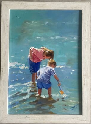 A young boy and girl bend over looking for fish in the shallow water at the edge of the ocean