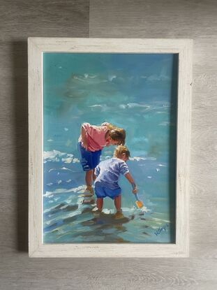 A young boy and girl bend over looking for fish in the shallow water at the edge of the ocean