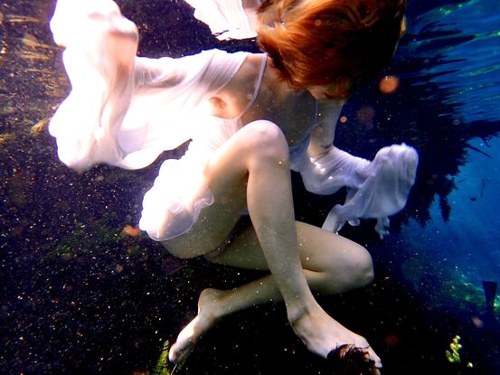 Young woman floating on the surface of the water  in a white dress - capturing beautiful reflections of light.