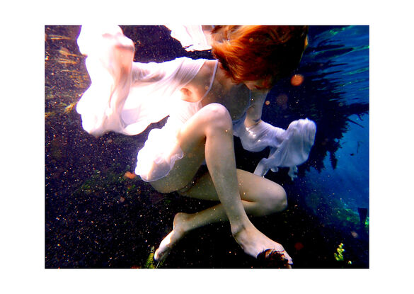 Young woman floating on the surface of the water  in a white dress - capturing beautiful reflections of light.