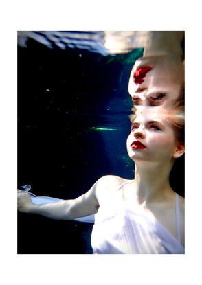 A surreal underwater scene where a girl in a white dress, who has light skin and blonde hair, is partially submerged in water and looks upon her reflection.