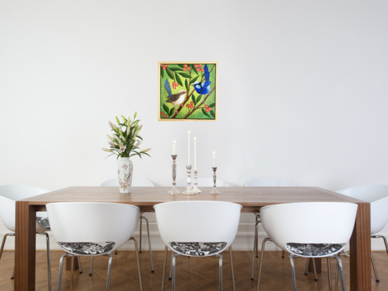 Two blue wrens, a male and a female, sitting in a tree surrounded by leaves and orange flowers. The background is a yellow-greenish colour which contrasts nicely with the blue of the birds and the orange flowers. The colour is wrapped around the sides of the canvas.