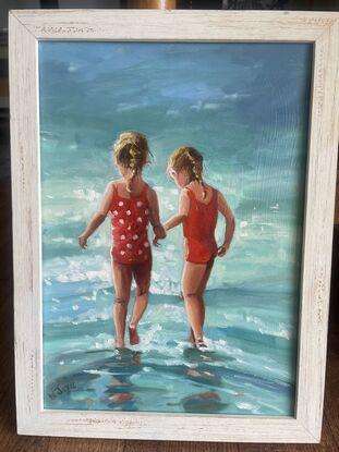 Two young girls in bright red bathers walk into a sparkling ocean