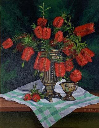 A vase of red bottlebrush on a green and white tablecloth.