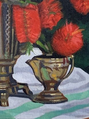 A vase of red bottlebrush on a green and white tablecloth.