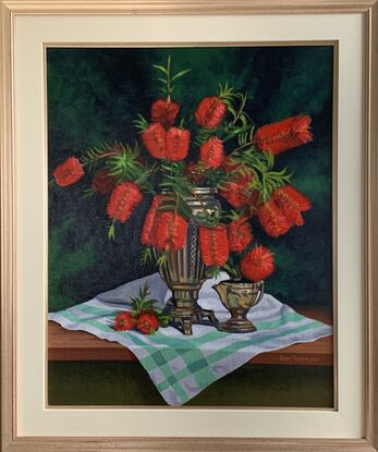 A vase of red bottlebrush on a green and white tablecloth.