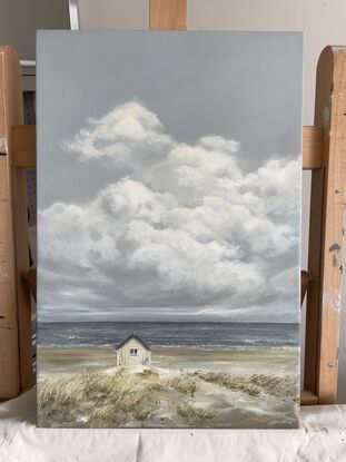 Lonely white shack on beach with puffy white clouds.