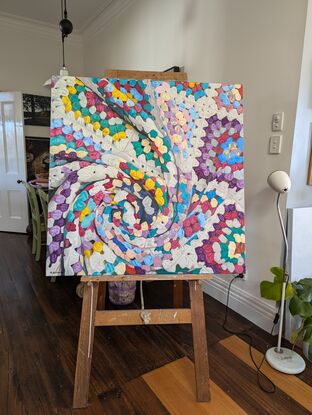 A crochet blanket folded into a swirl, that looks almost like an abstract painting with many colours, texture and depth.