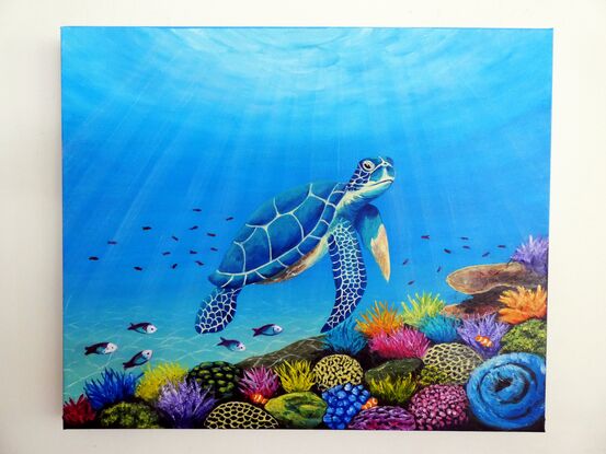 A blue green sea turtle swimming over a multi-coloured coral reef with sunlight shining down through the water. The coral is yellow, blue, purple and pink coloured with green and pink parrot fish and clown fish and other small tropical fish swimming over the reef.