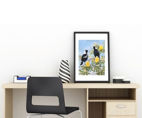 Two glossy black and white magpies perch amongst a mass of yellow coastal banksia flowers and their leathery, twisting leaves, against a blue sky.