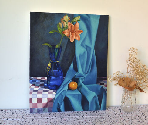 Orange lily in blue vase and an orange mandarin trying to hide in a silky turquoise blue fabric