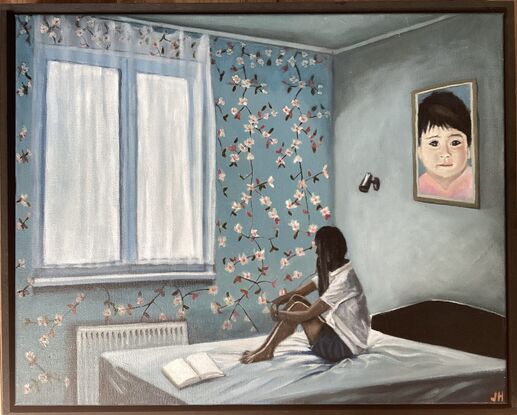 A girl sits on a bed hugging her knees beside a window  in a room decorated with floral wallpaper and a large portrait of a young child. At her feet are the open pages of a blank book.