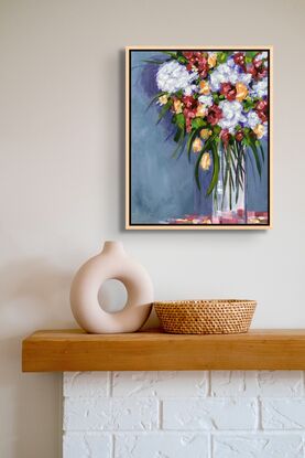 A bouquet of flowers in a tall glass Vase,  A blue grey wall with soft shadows.