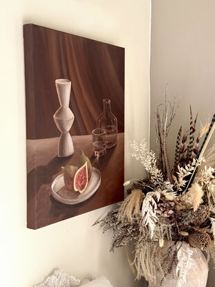 A side lit table scene with long shadows & a beam of light. A plate with figs in the foreground with a white modern vase, glass bottle and drinking glass with water in it.