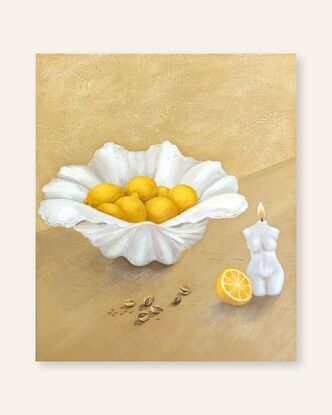 A clam shell holding juicy lemons sits behind scattered pistachios and a lit candle in the shape of a woman on a textured beige yellow background.