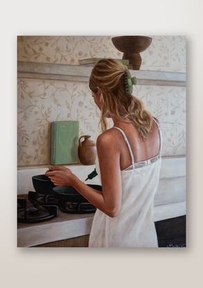 Young lady with her back to the camera, wearing a white linen dress and cooking in a kitchen