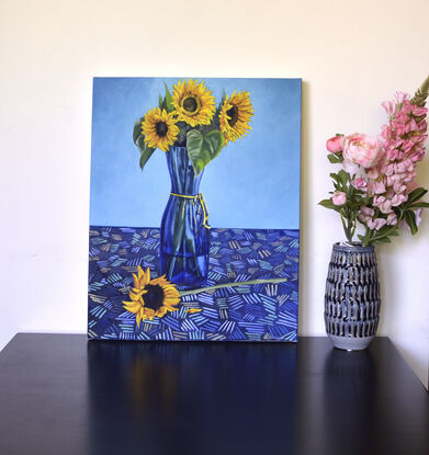 Golden yellow sunflowers in blue glass vase kept on a patterned table cloth   