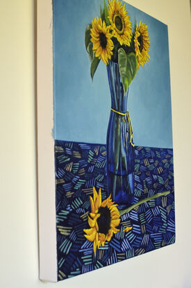 Golden yellow sunflowers in blue glass vase kept on a patterned table cloth   