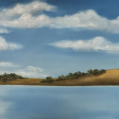 Lake bordered by hills and trees and reflecting blue sky and clouds.