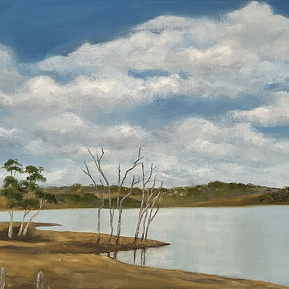 Lake bordered by hills and trees and reflecting blue sky and clouds.