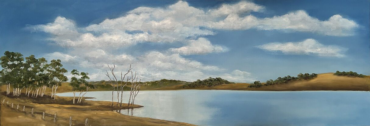 Lake bordered by hills and trees and reflecting blue sky and clouds.