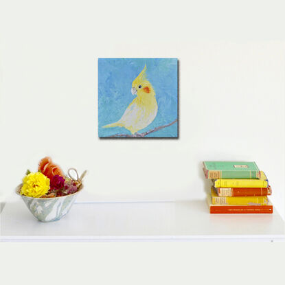 Oil painting portrait of a pet Cockatiel Parrot. This medium sized bird is bright yellow with a yellow crest and orange spot on his face. The background is textured blue.