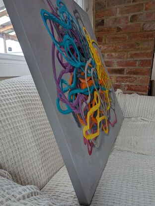 A birds eye view of a colourful pile of woollen threads on a grey background.