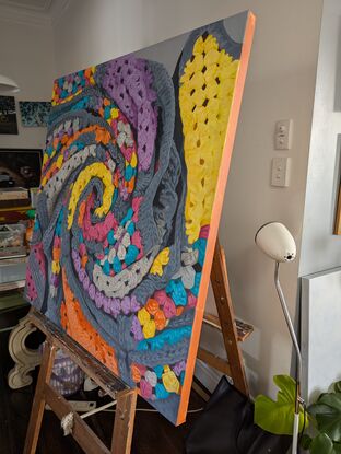 A crochet blanket folded into a swirl, that looks almost like an abstract painting with many colours, texture and depth.