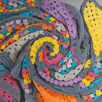 A crochet blanket folded into a swirl, that looks almost like an abstract painting with many colours, texture and depth.